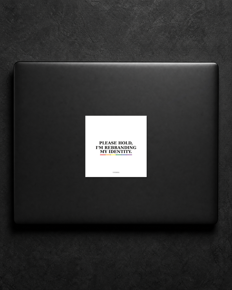 Please Hold, I'm Rebranding My Identity sticker centered on a black laptop lid.