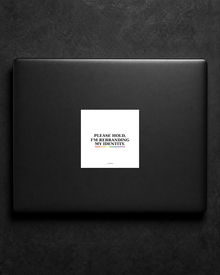 Please Hold, I'm Rebranding My Identity sticker centered on a black laptop lid.